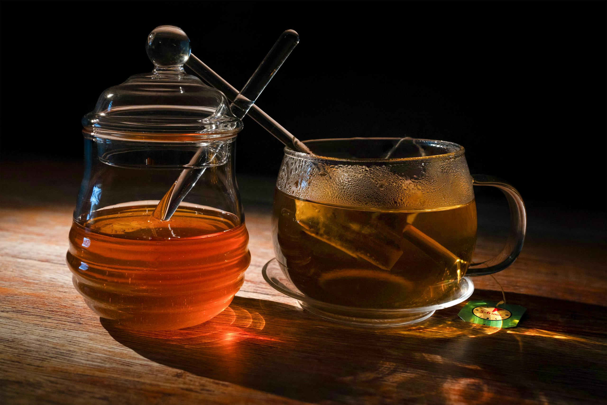 A cozy setting featuring a steaming cup of herbal tea beside a honey jar on a wooden table, perfect for relaxation.