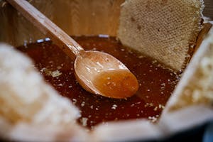 Close-up of fresh honey and honeycomb with a wooden spoon in a rustic wooden bowl.