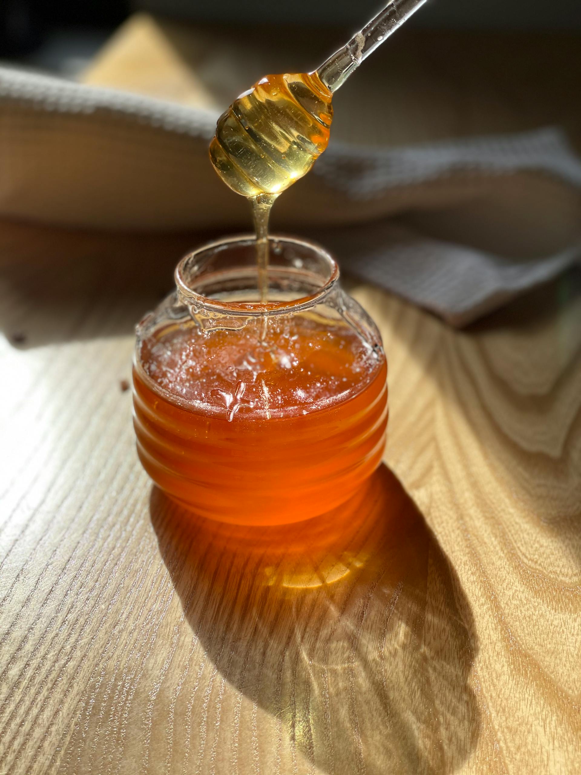 Close-up of honey drizzling into a glass jar on a wooden table, ideal for food and lifestyle themes.