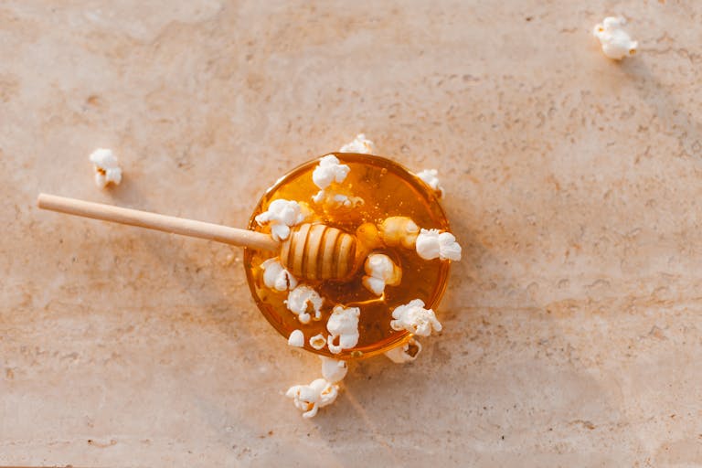 Top view of honey drizzler with popcorn on marble, perfect culinary texture.