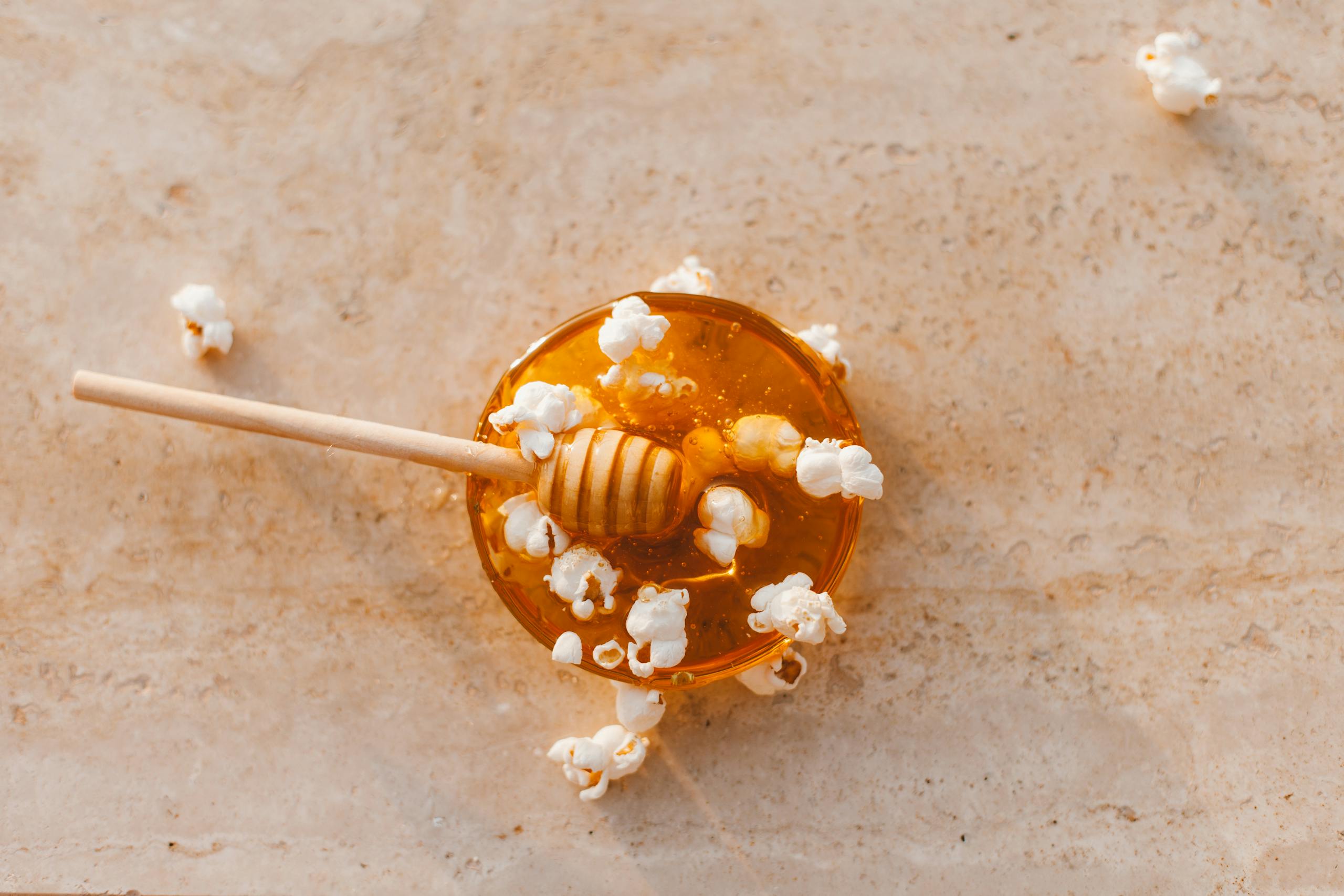 Top view of honey drizzler with popcorn on marble, perfect culinary texture.